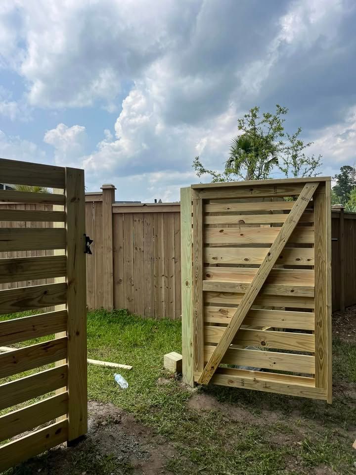 A wooden gate is sitting in the grass next to a wooden fence.