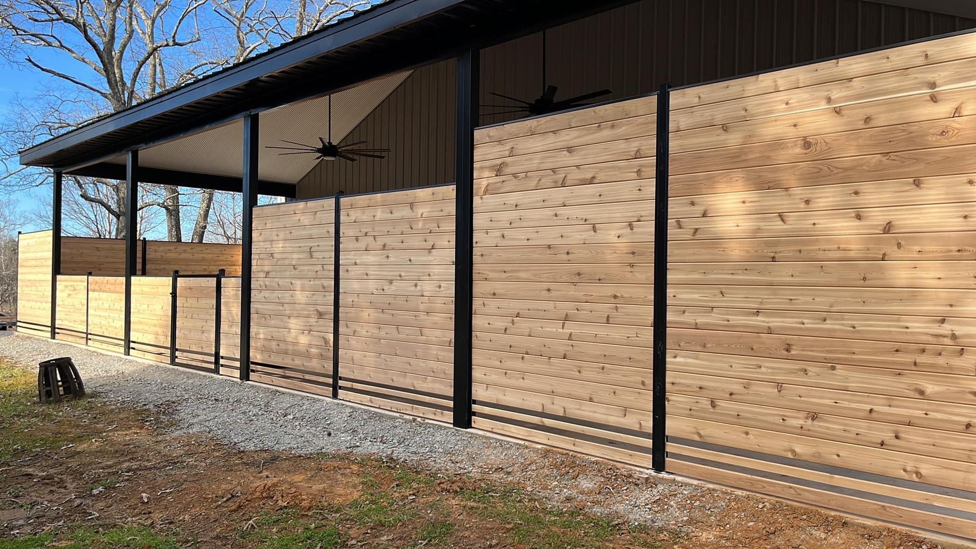 A wooden fence is surrounding a building with a black roof.