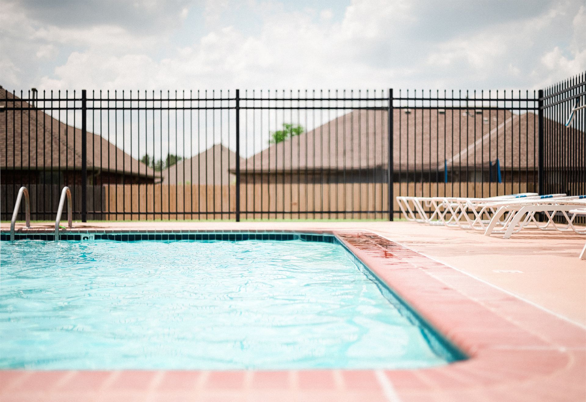 A swimming pool surrounded by a metal fence and chairs.