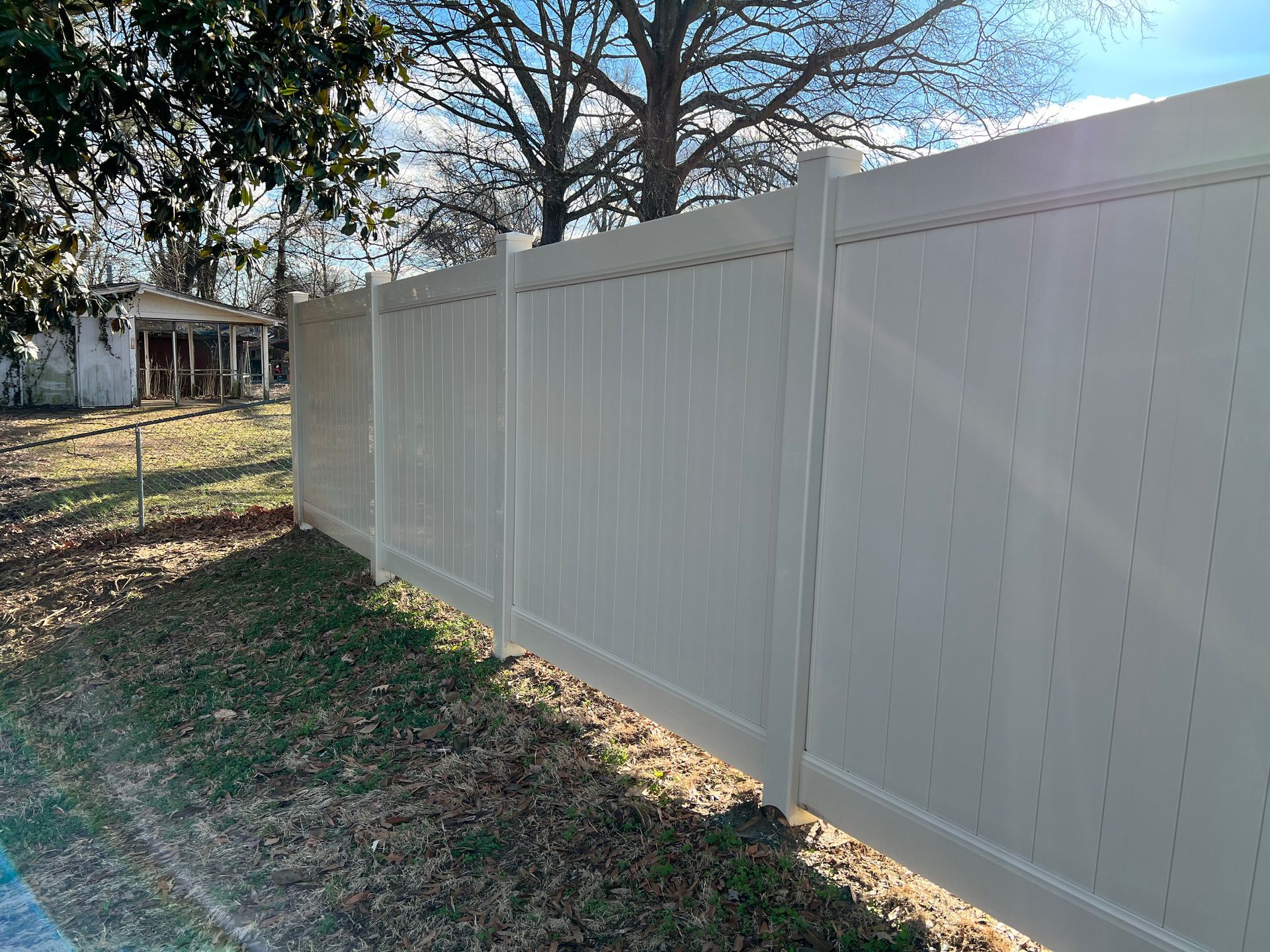 A white vinyl fence surrounds a yard with a house in the background.