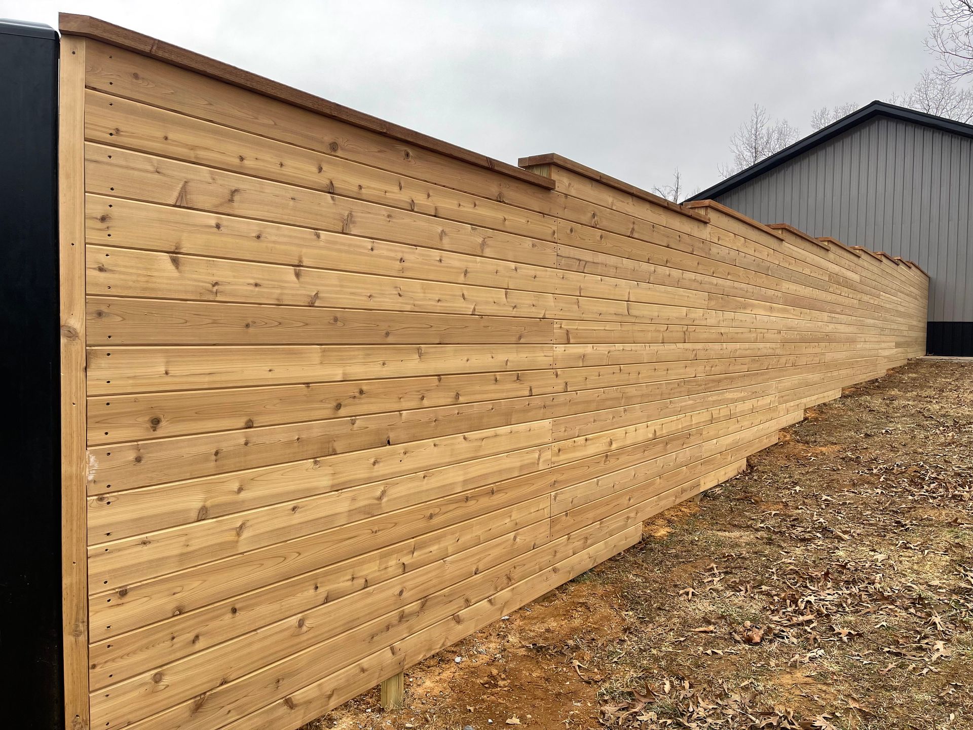 A wooden fence is sitting on top of a dirt hill next to a building.