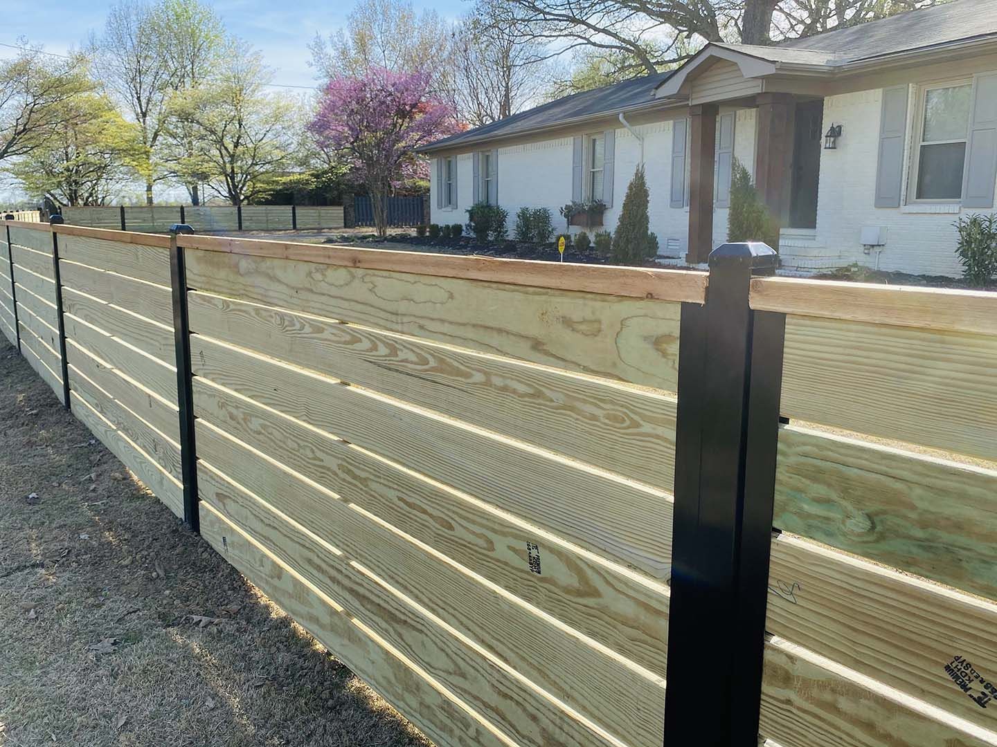 A wooden fence is sitting in front of a white house.