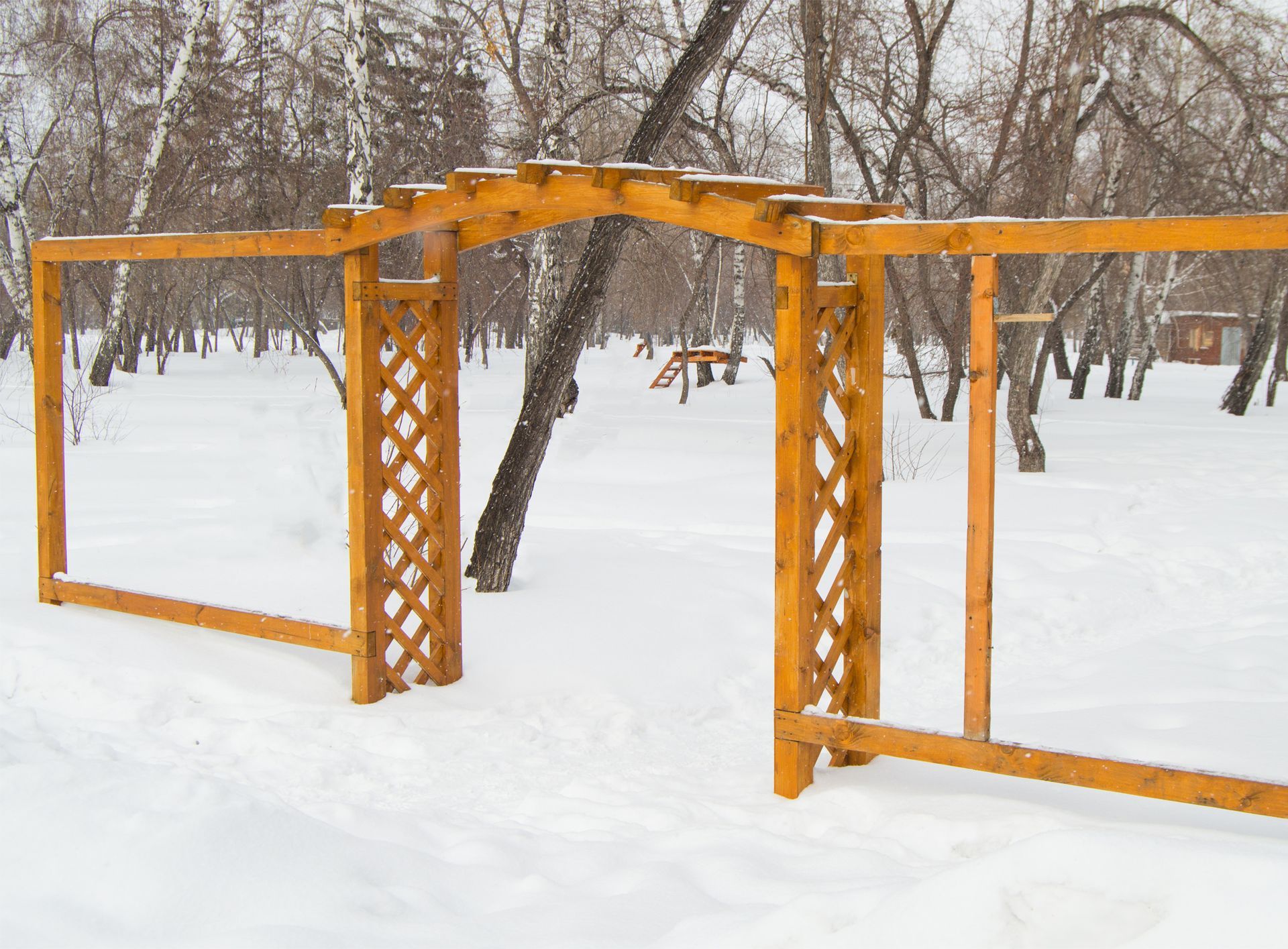 A wooden archway in the snow in a park.