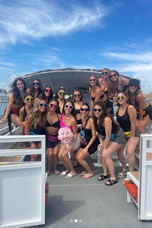 Group of women on a boat smiling and posing, bright sunny day, blue sky, holding a face cutout.