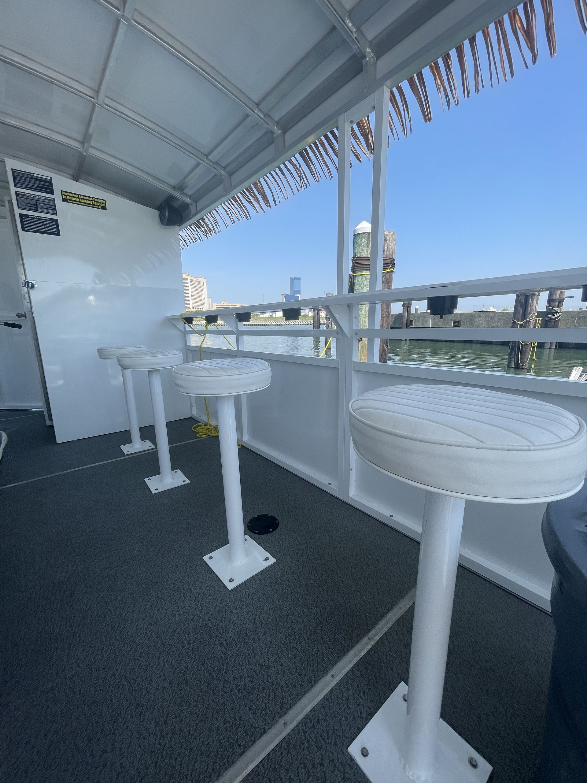 Three white bar stools on a boat deck, with a harbor view in the background.