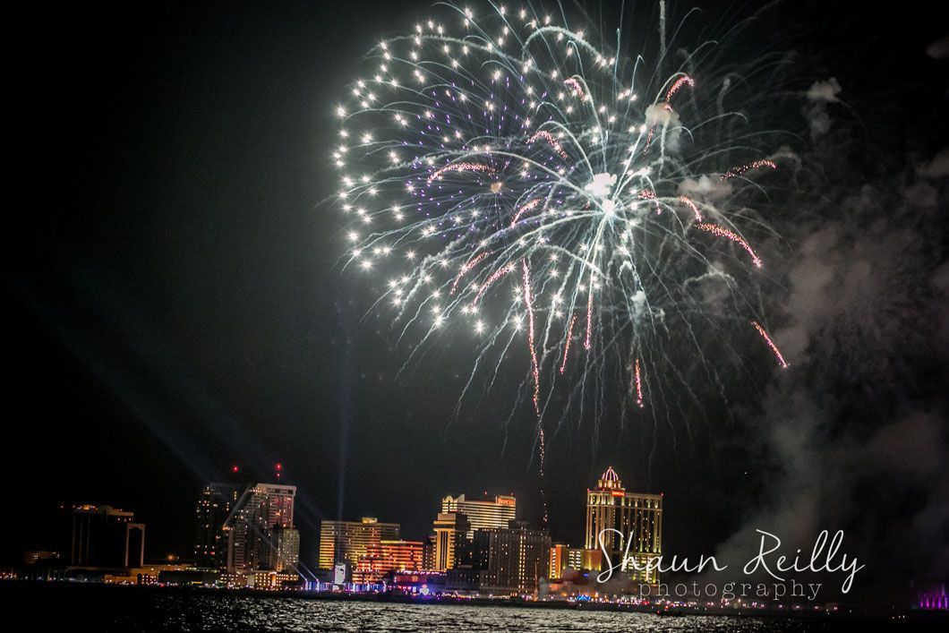 Fireworks burst over a brightly lit cityscape at night.