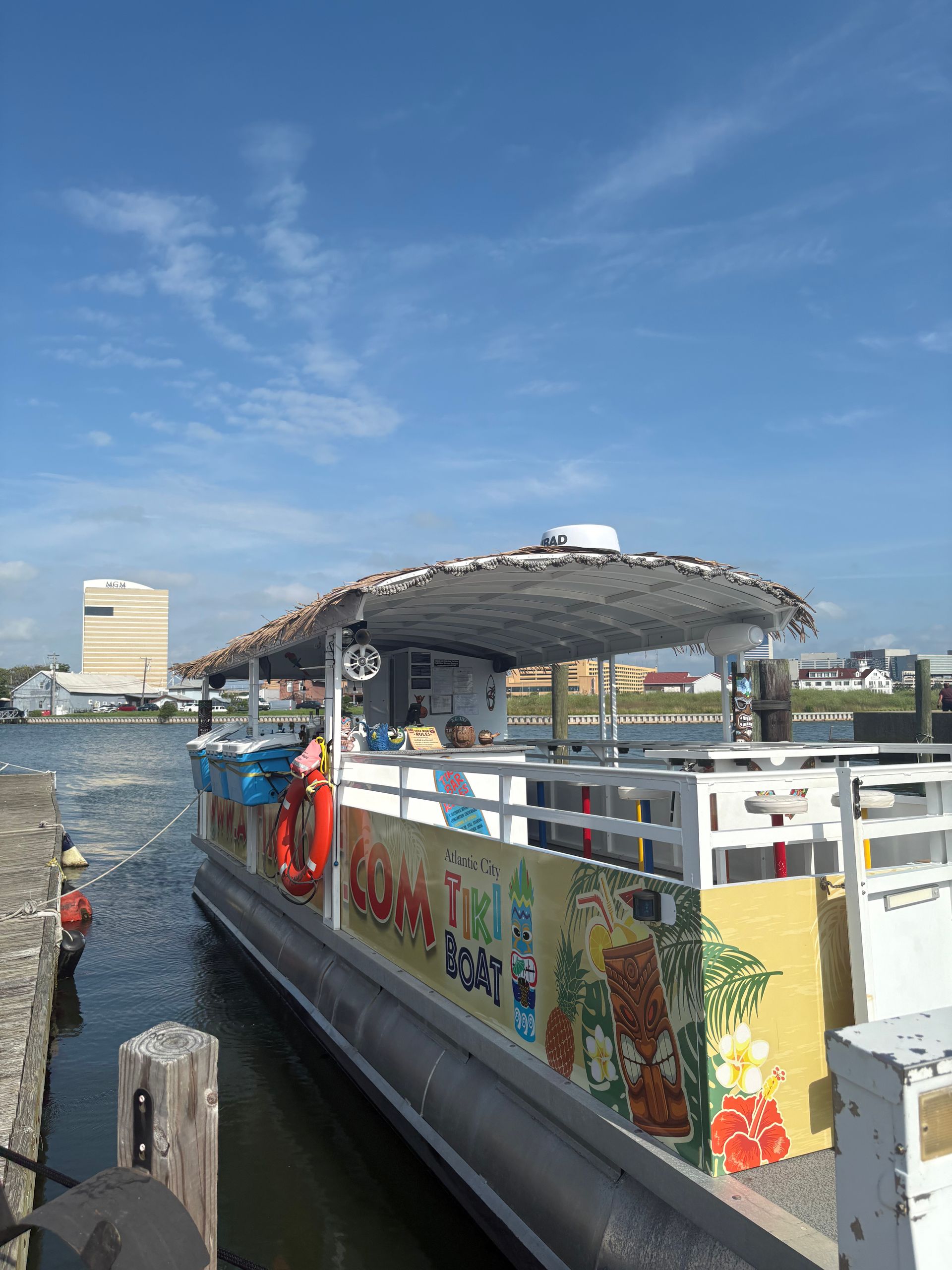 A colorful party pontoon boat docked at a pier under a bright blue sky.