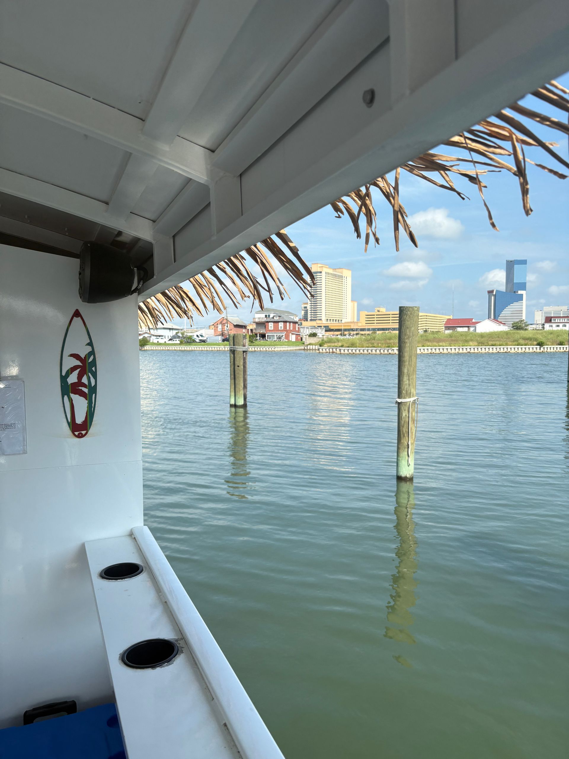 View from a boat with a tiki-style roof over water, looking towards buildings on the horizon.