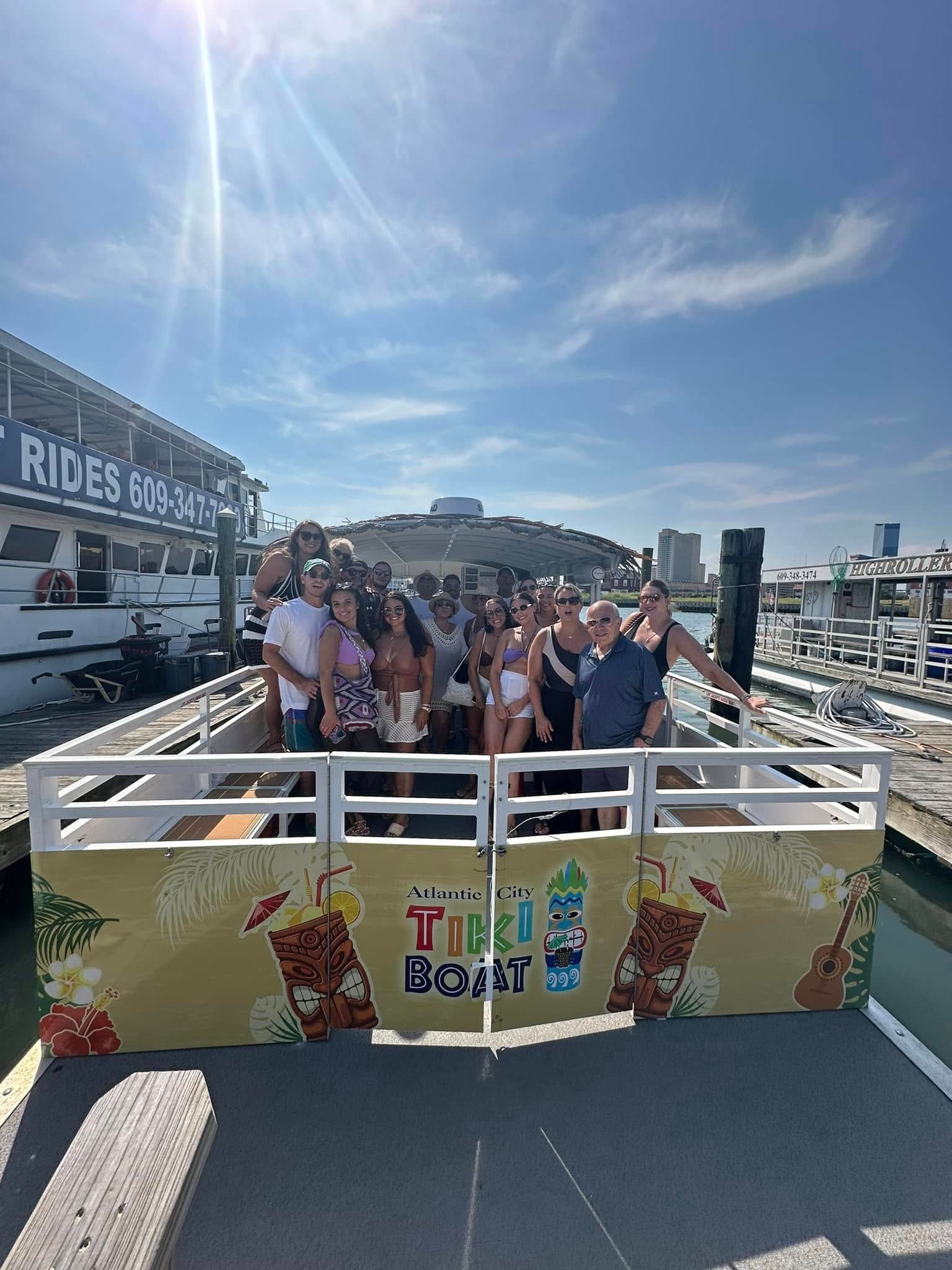 Group on a tiki boat, smiles, sunny day. Building and dock in background.