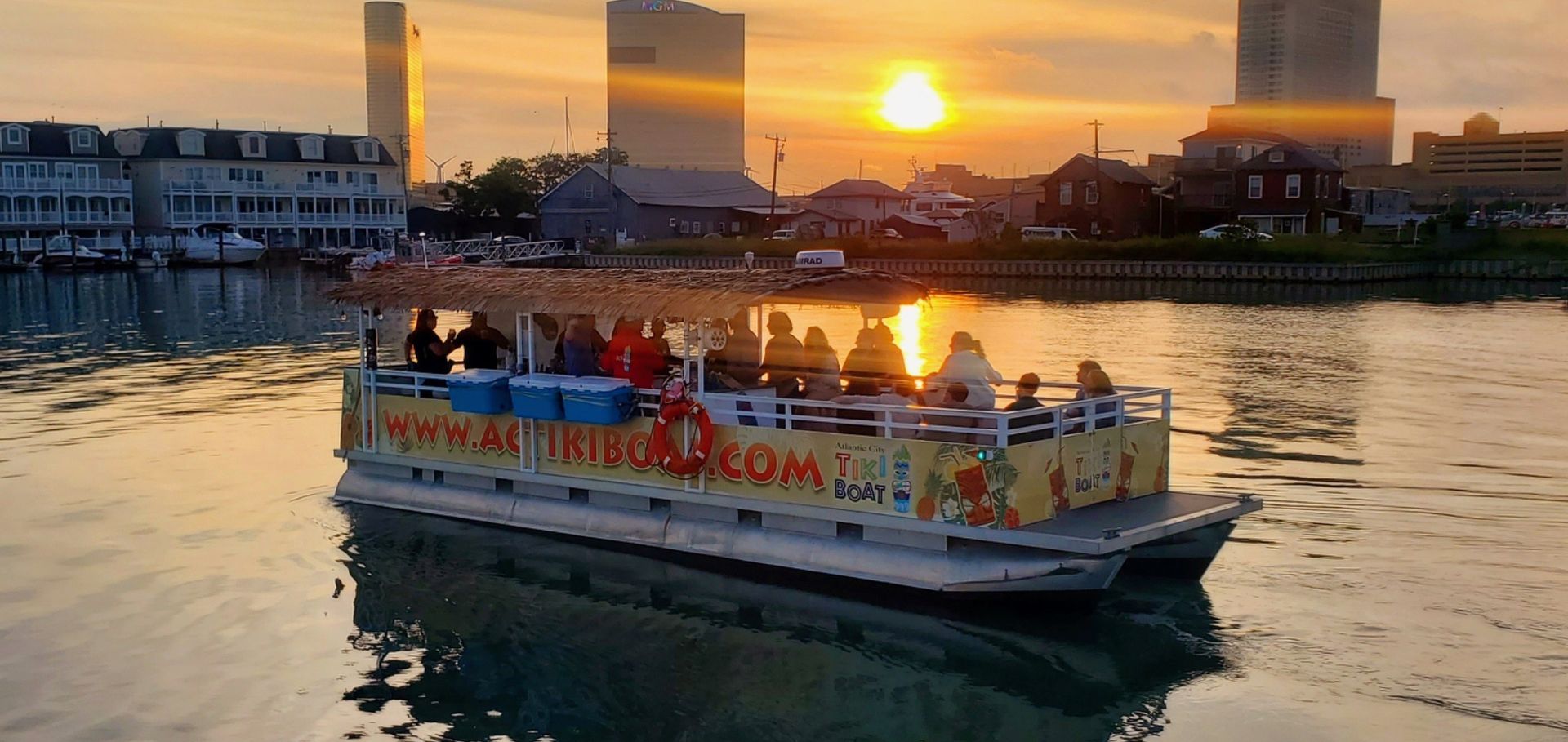 A boat with people on it sails on the water at sunset in a city.