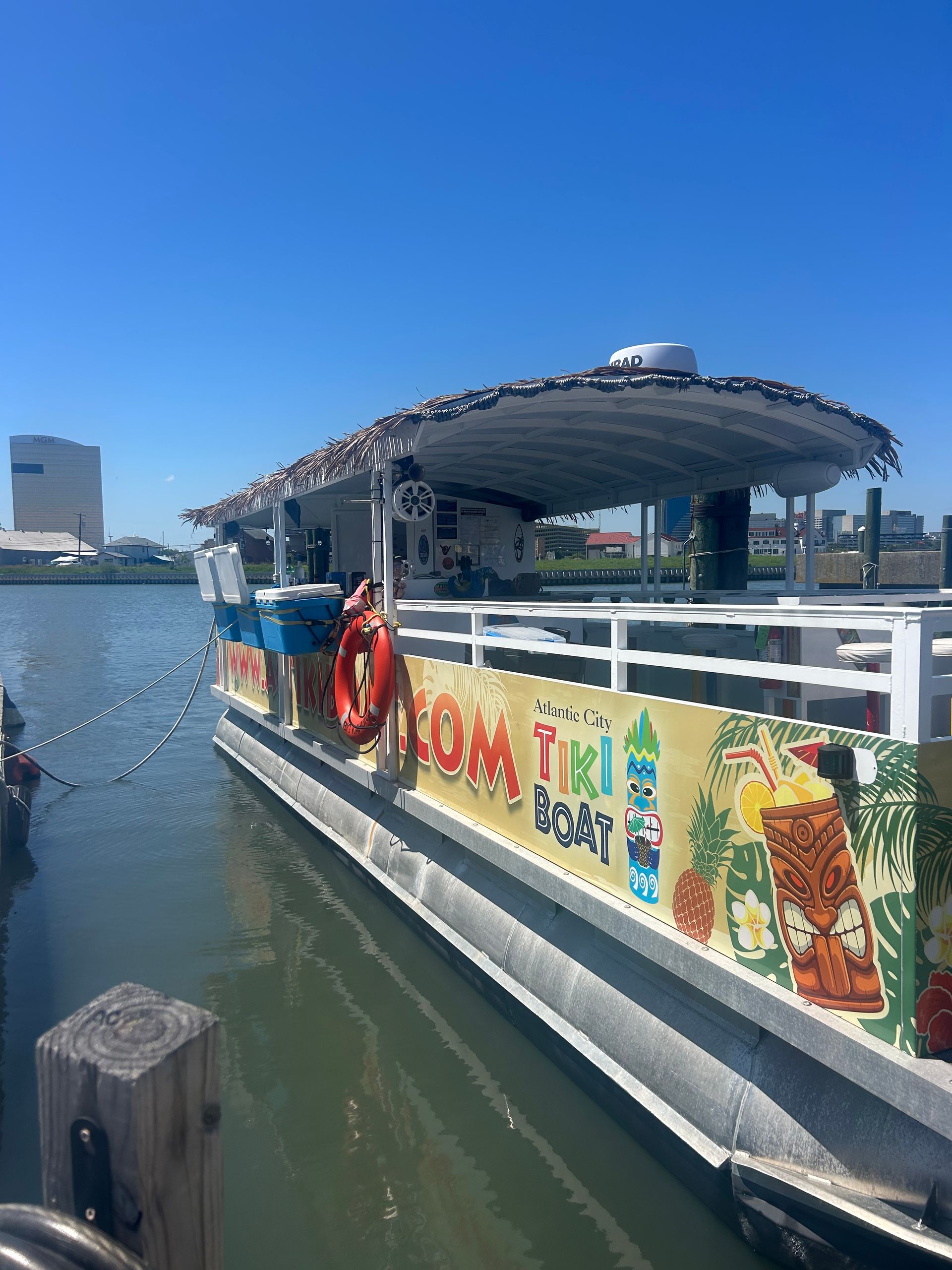 A tiki-themed boat docked at a pier, with signage and a thatched roof, under a blue sky.