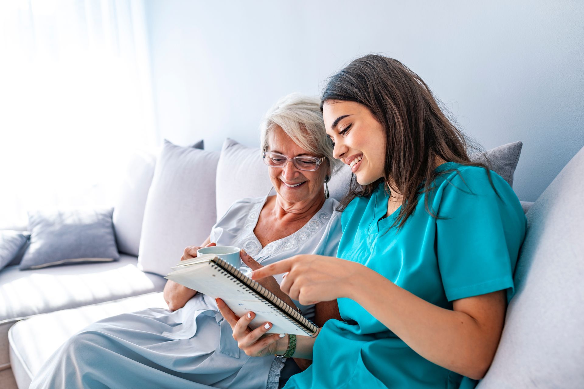 Caregiver and senior woman on a couch looking at a tablet together