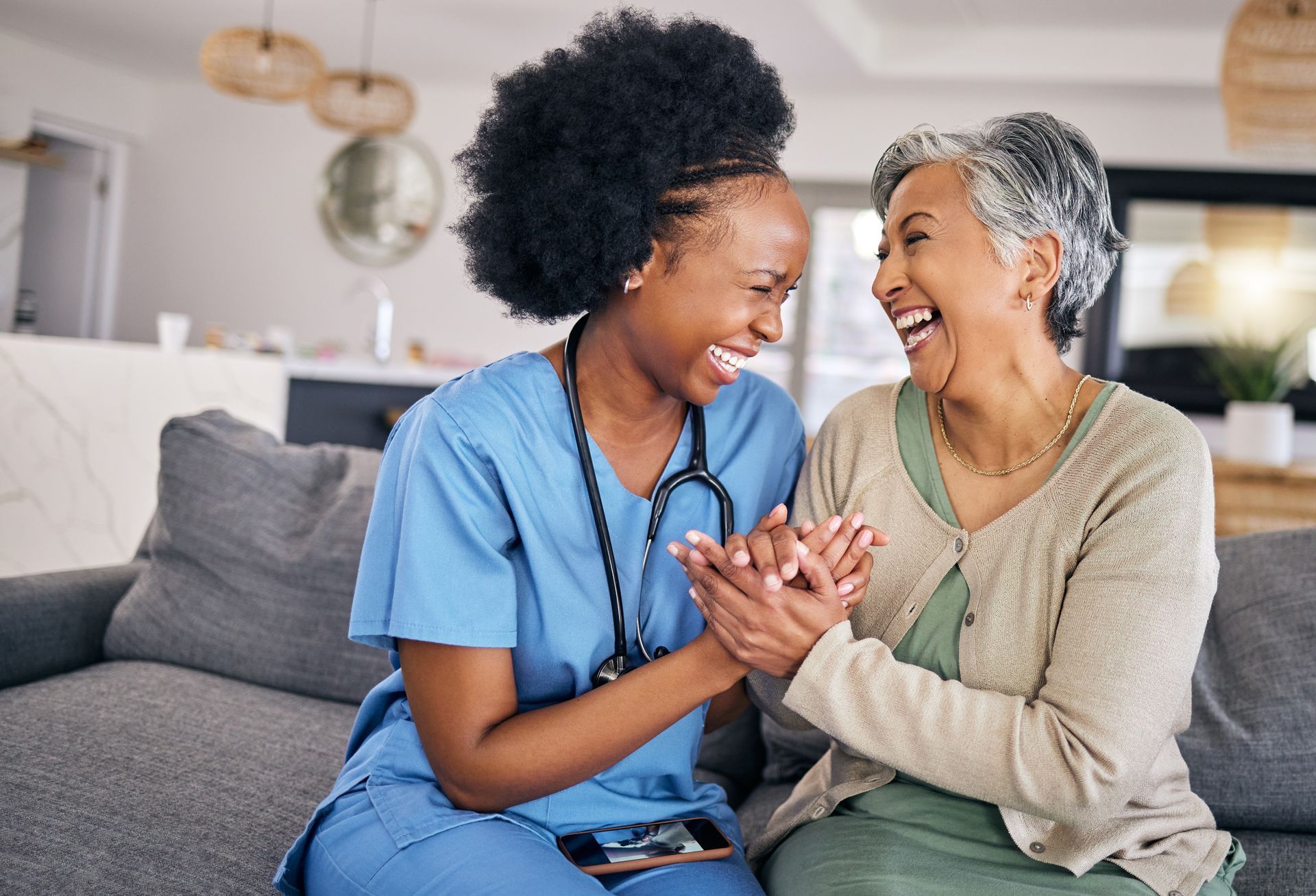 A healthcare worker in blue scrubs laughs with an elderly person