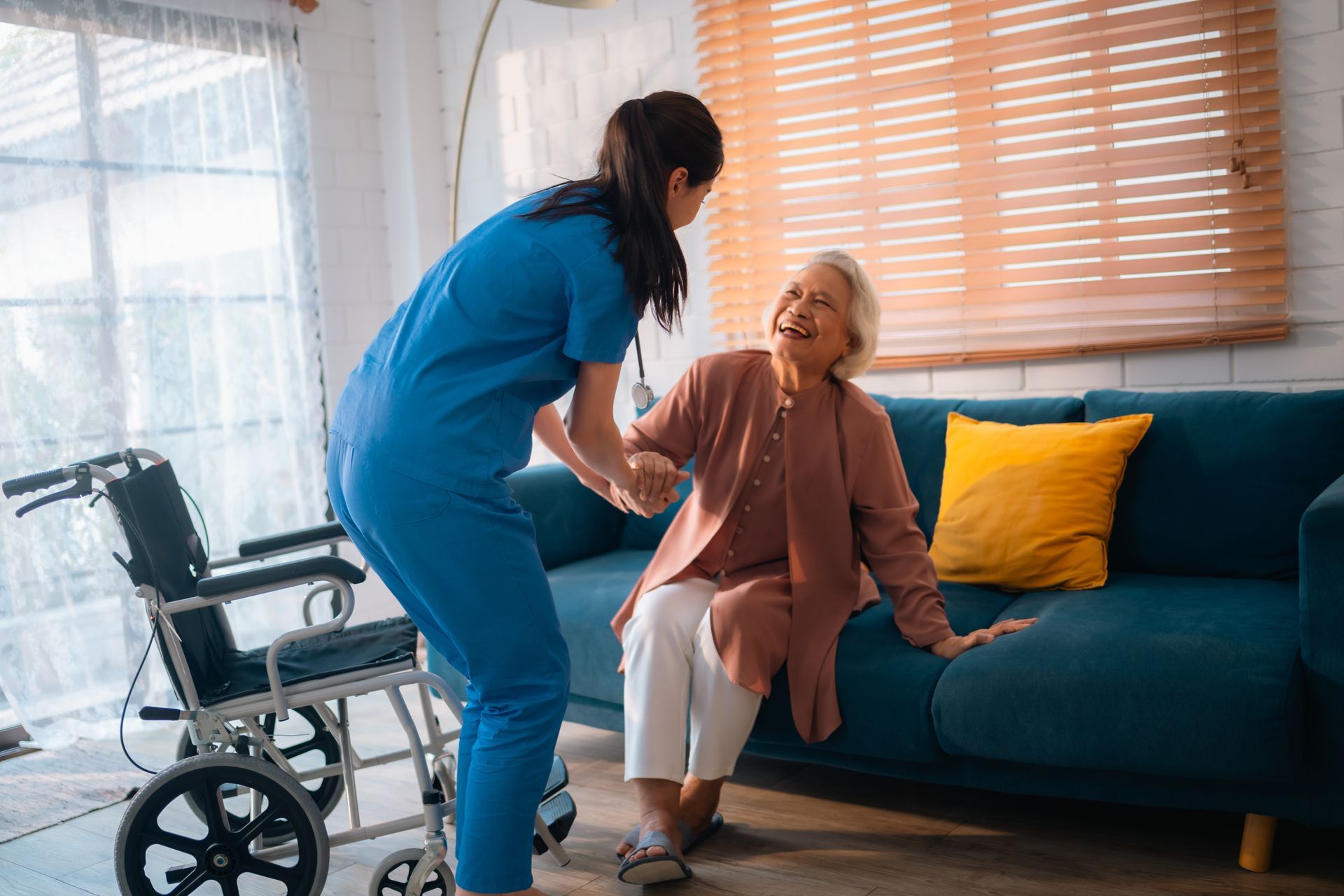 Caregiver helping a person sit up on a blue couch in a well-lit living room