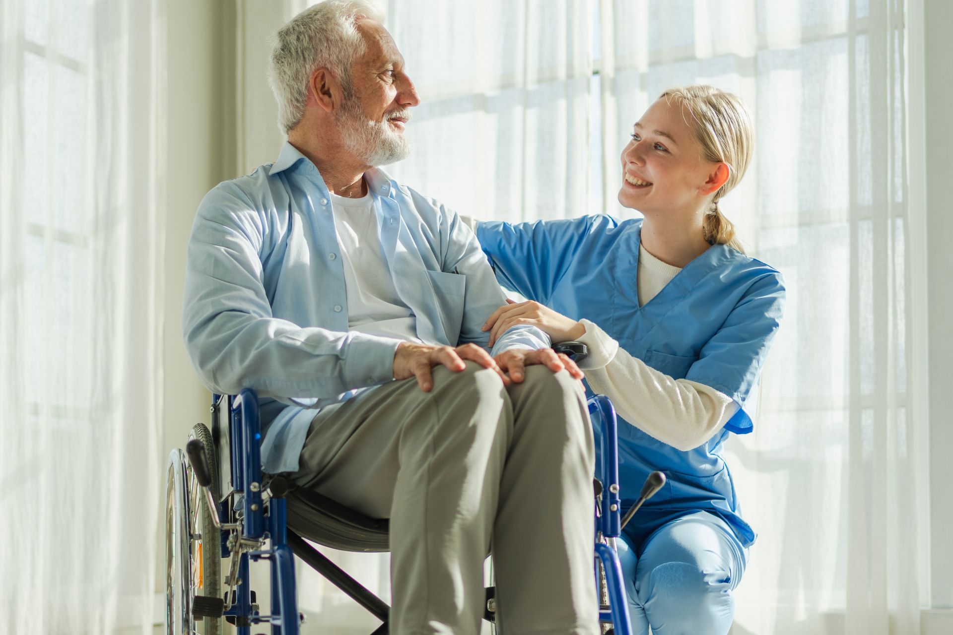 A smiling caregiver in scrubs assists an elderly man