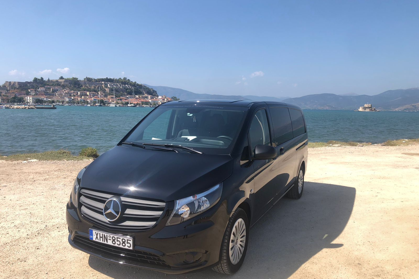 Athenaos premium Mercedes van parked by the seaside with mountains in the background.