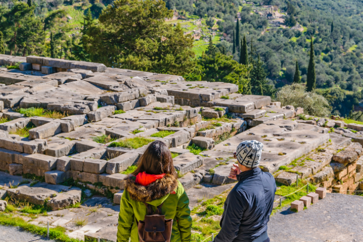 Tourists exploring the ancient ruins of Delphi with mountain views
