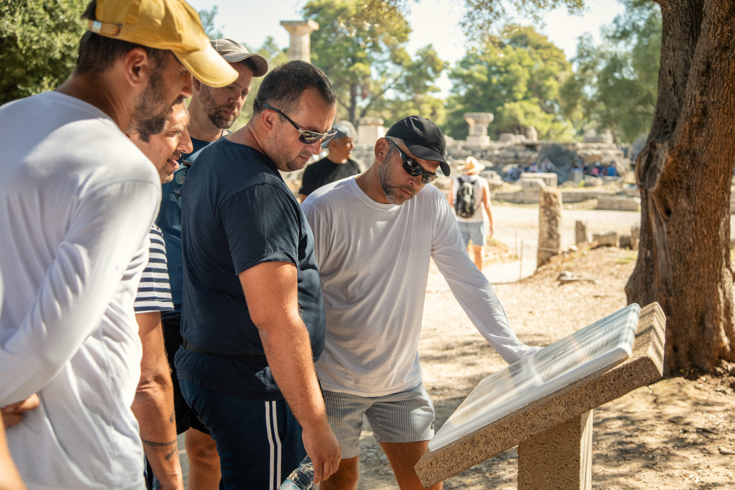 Visitors exploring ancient ruins and reading information signs at the archaeological site of Olympia