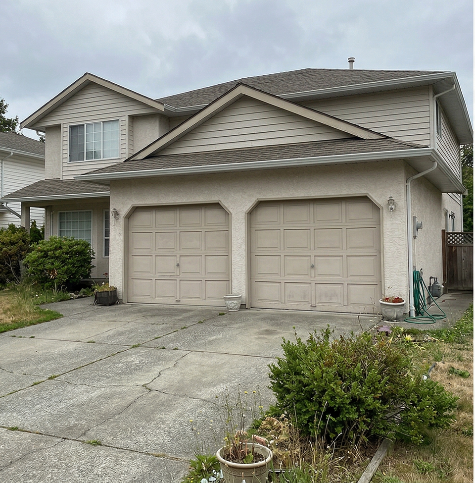 A beige two-story suburban house with a two-car garage and a cracked concrete driveway under a cloudy sky.