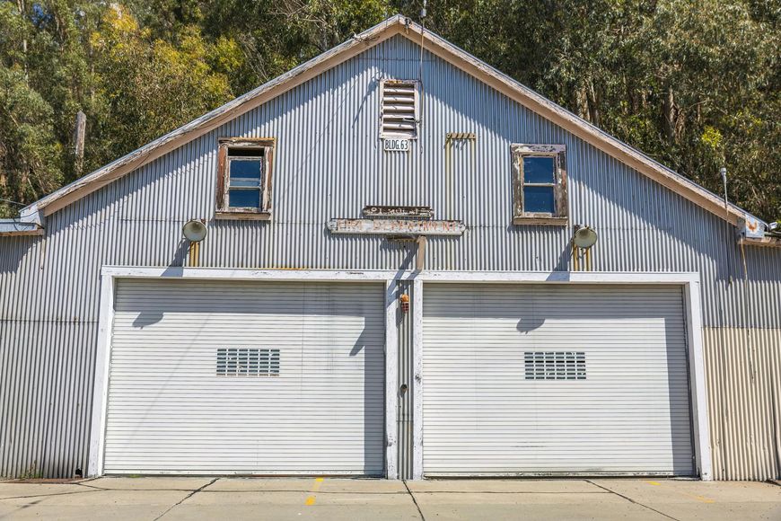 A light-blue, metal-sided building with two large garage doors, two small windows, and a vent under a peaked roof.