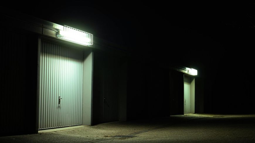 Two industrial-style storage units with bright overhead lights illuminate closed metal doors at night.