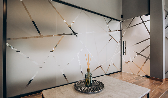 A frosted glass wall with geometric metallic lines in a modern room, featuring a small vase on a table in the foreground.