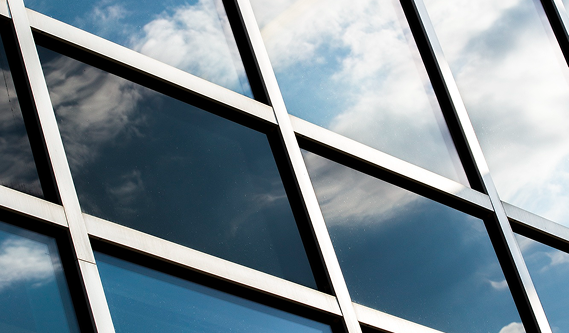 Reflections of a blue, cloudy sky on the dark, square glass panes and metal grid of a modern building facade.