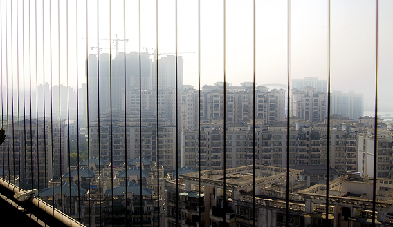 View of a dense residential city through a vertical cable safety balcony railing on a hazy, overcast day.