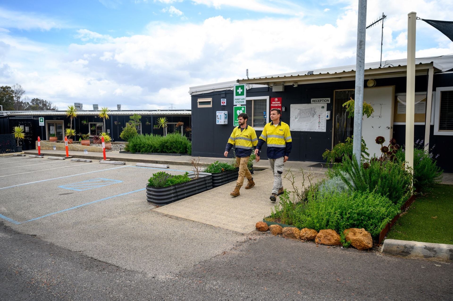 Two men walking side-by-side on a walkway between buildings in a work site setting.