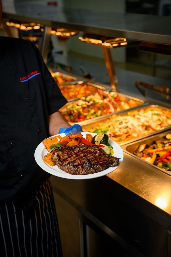 Chef holding a plate of steak, sweet potatoes, and vegetables in the Collie Hills Village cafeteria.