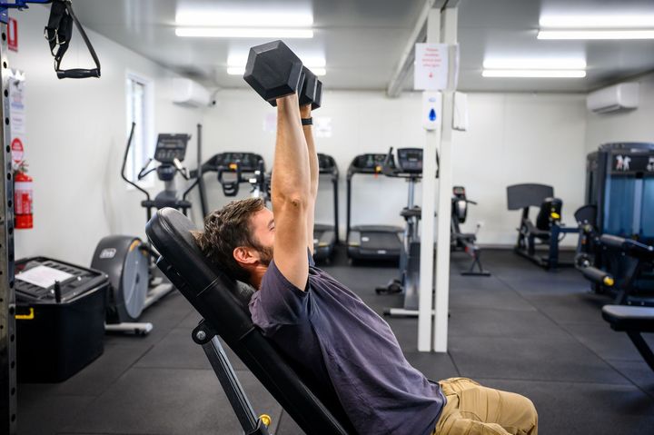 Man lifting dumbbells on an inclined bench in a gym at Collie Hills Village.