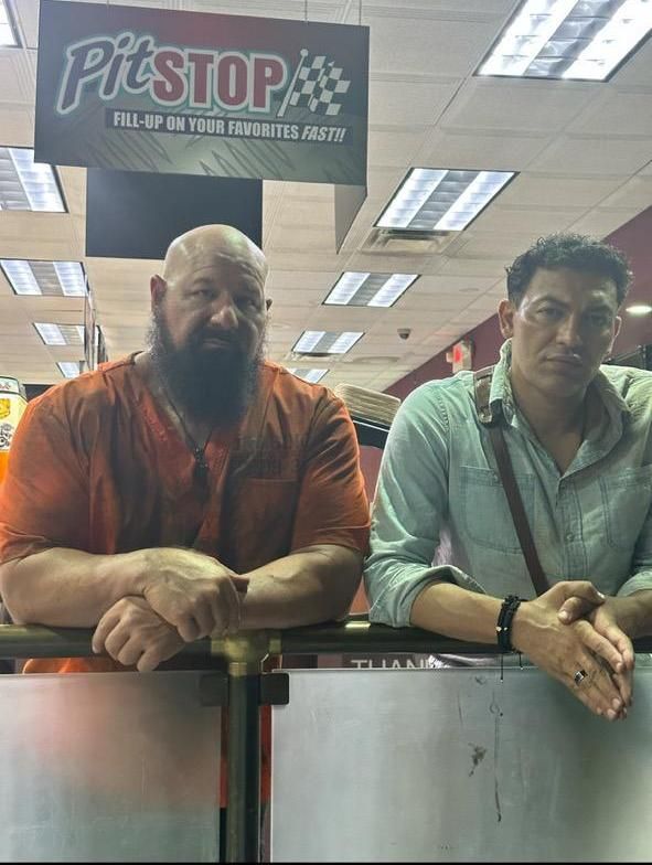 Two men standing next to each other under a sign that says pitstop.