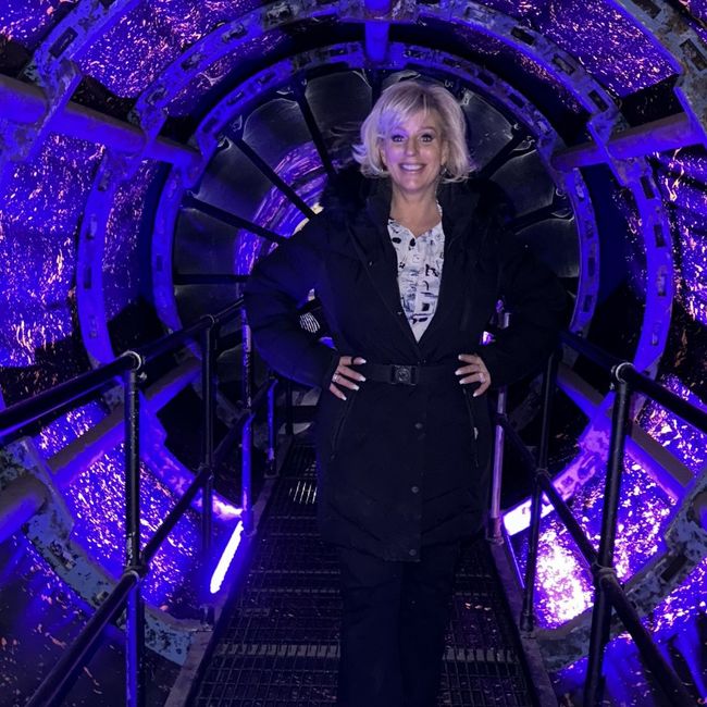 A woman in a black coat is standing in a purple tunnel.