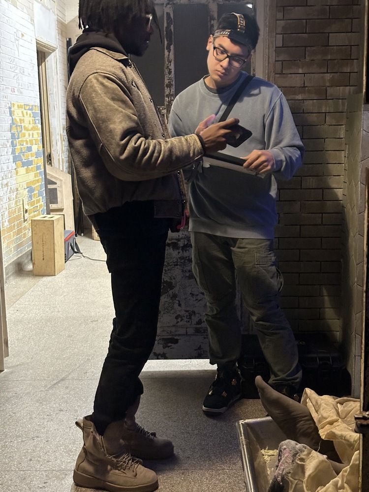 Two men are standing next to each other in a hallway looking at a tablet.