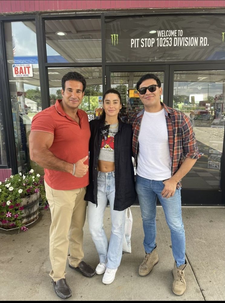 Three people are posing for a picture in front of a gas station.