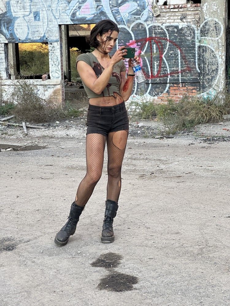 A woman in a crop top and shorts is standing in front of a building with graffiti on it.
