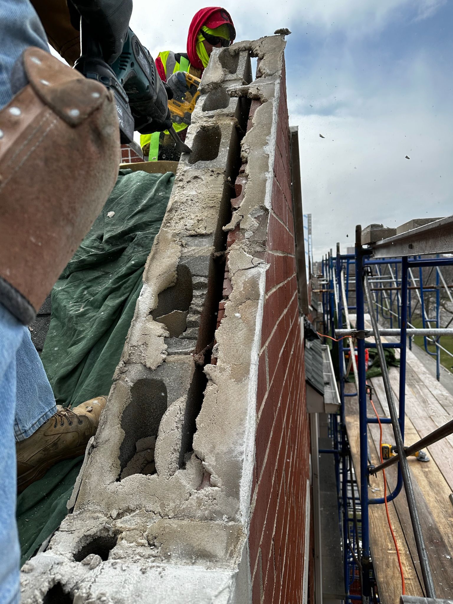 Workers removing damaged parts of brick parapet wall on rooftop