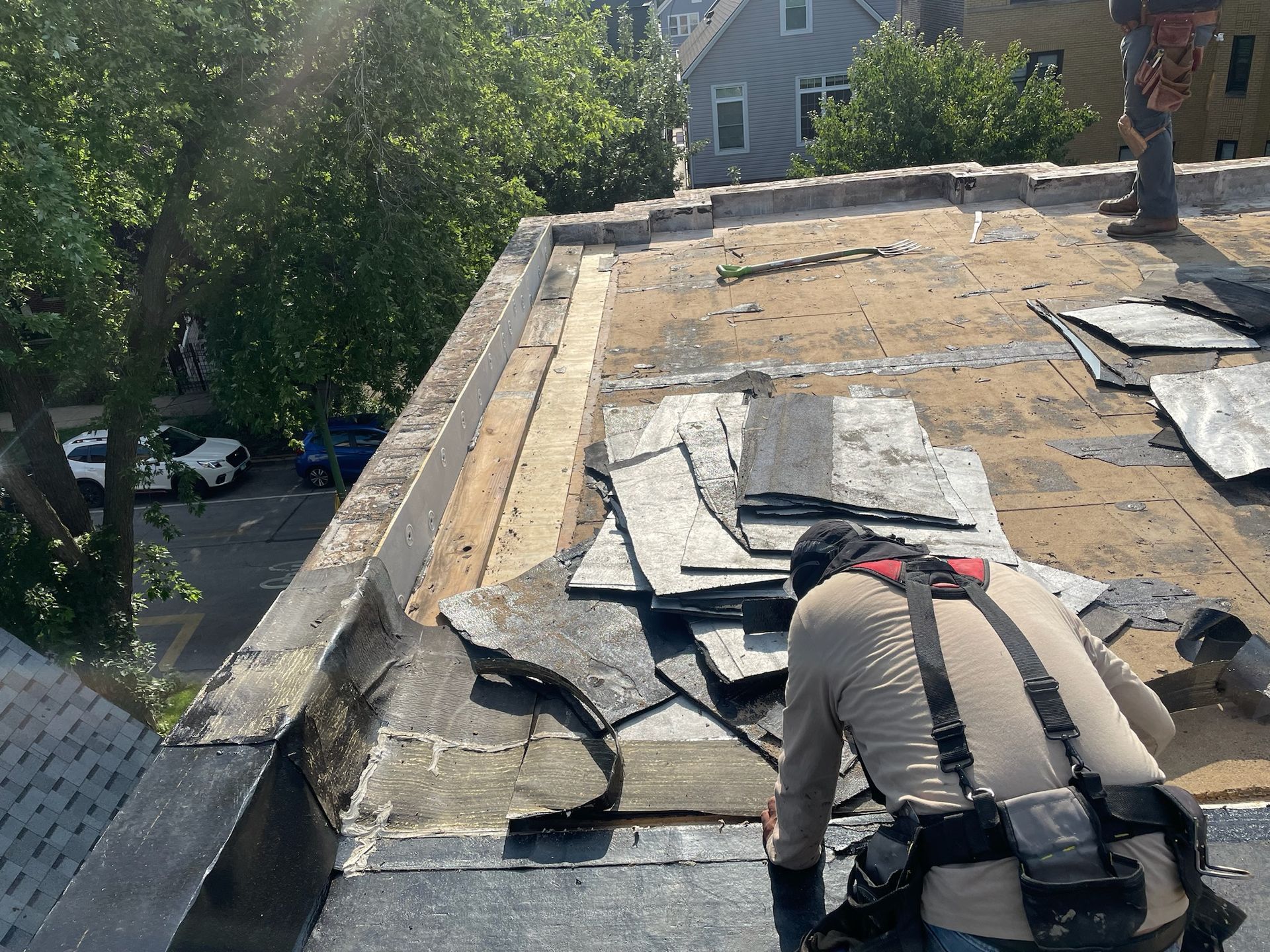 Worker tearing off rooftop surface exposing damaged roof wood material