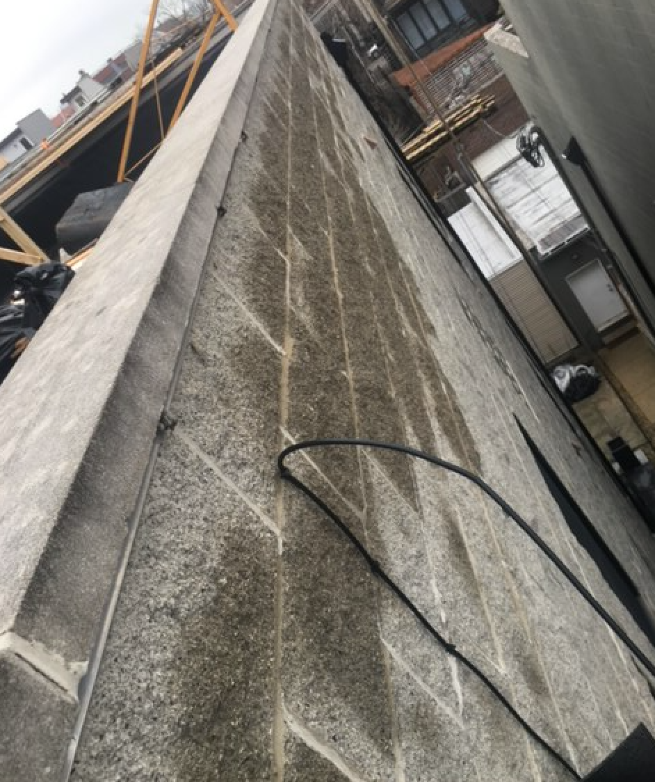 Water rushes to the top of split face block parapet wall after WickRight capstone vented drip edge is installed in West Town, Chicago