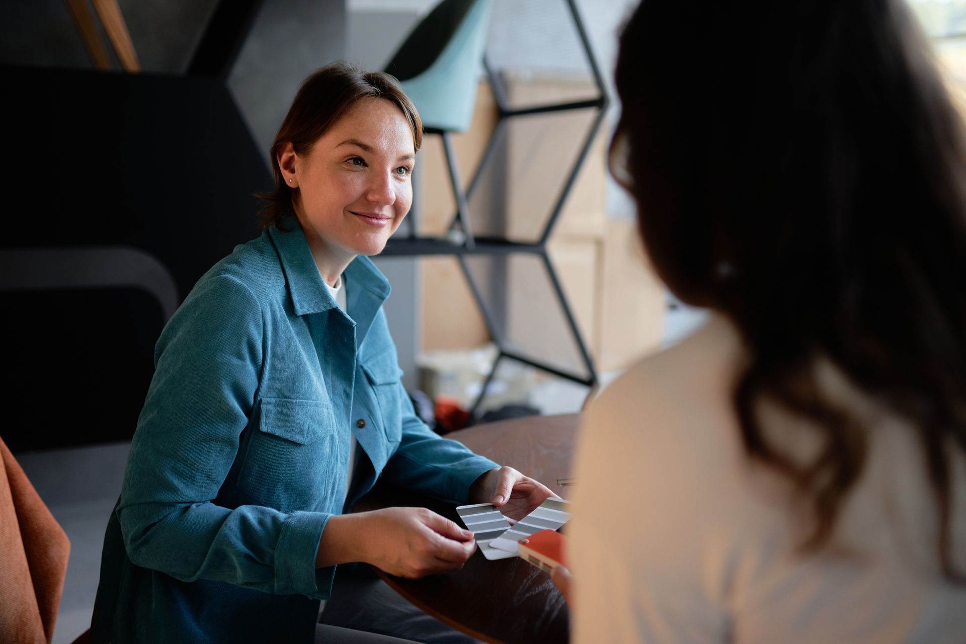 A woman smiles while showing color samples to another woman.