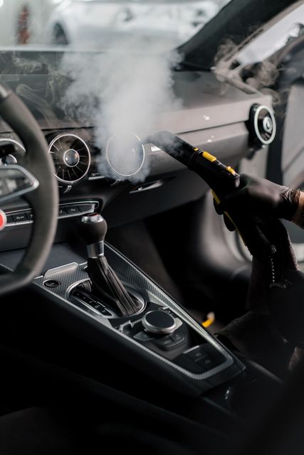 Car interior with steam from the dashboard and a handheld device cleaning or disinfecting the center console