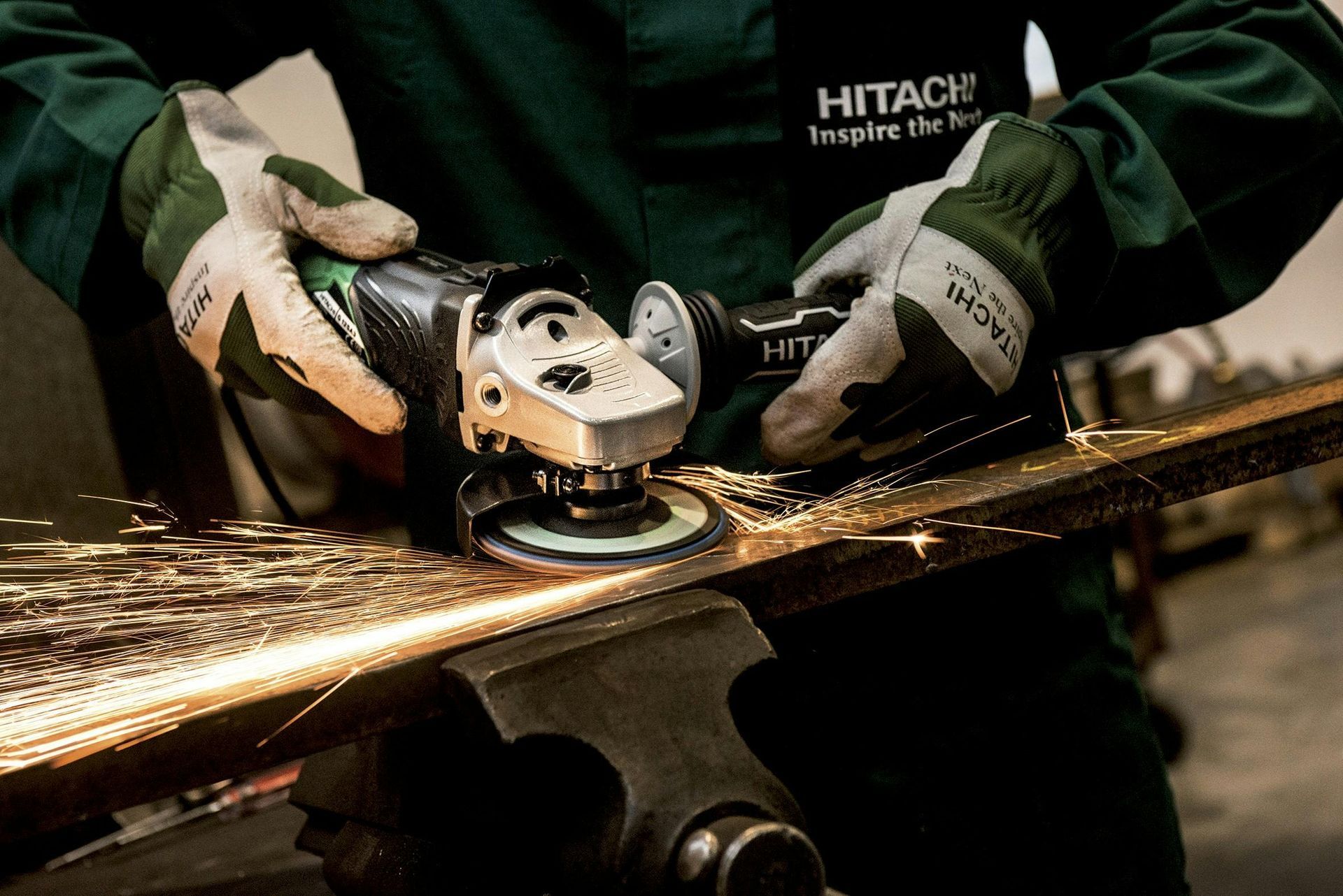 A person wearing work gloves using a Hitachi angle grinder to cut metal, creating sparks.