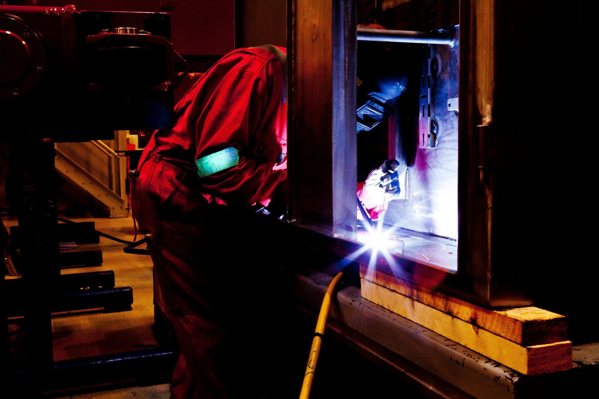 Welder in red protective clothing, welding near a window frame.