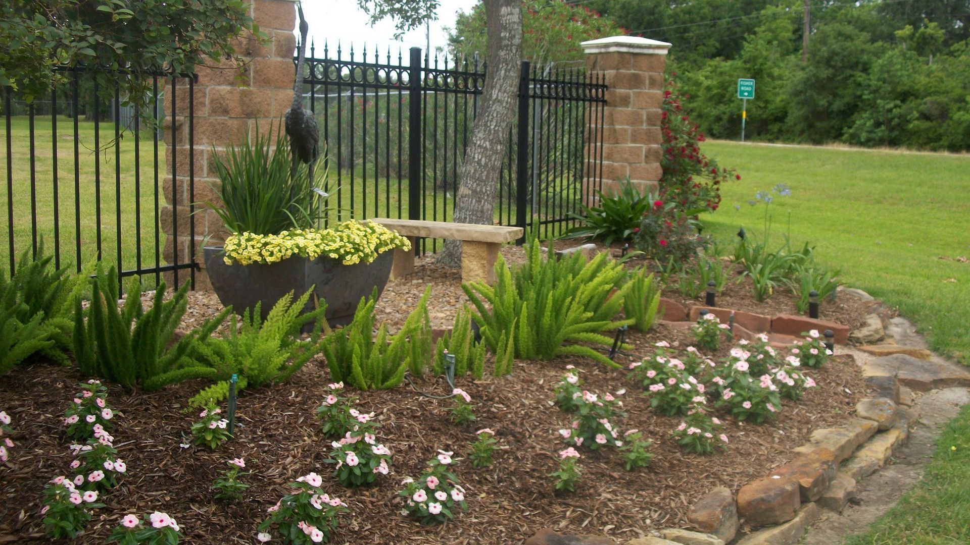 A garden with flowers and a bench in front of a fence