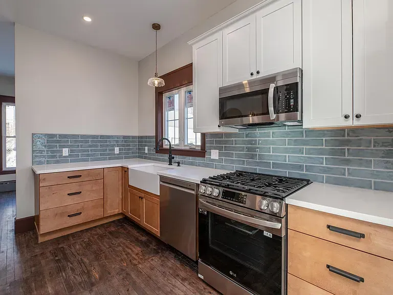 Modern kitchen with light wood cabinets, stainless steel appliances, and blue tile backsplash.