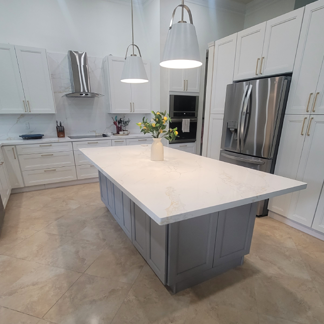 Modern white kitchen with gray island, stainless steel appliances, and pendant lights.