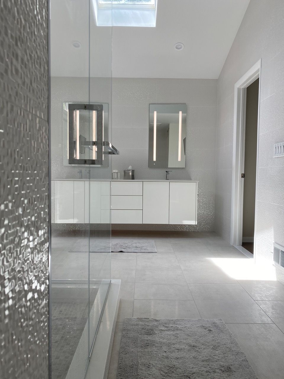 Modern bathroom with floating white vanity, two lighted mirrors, and a glass shower.