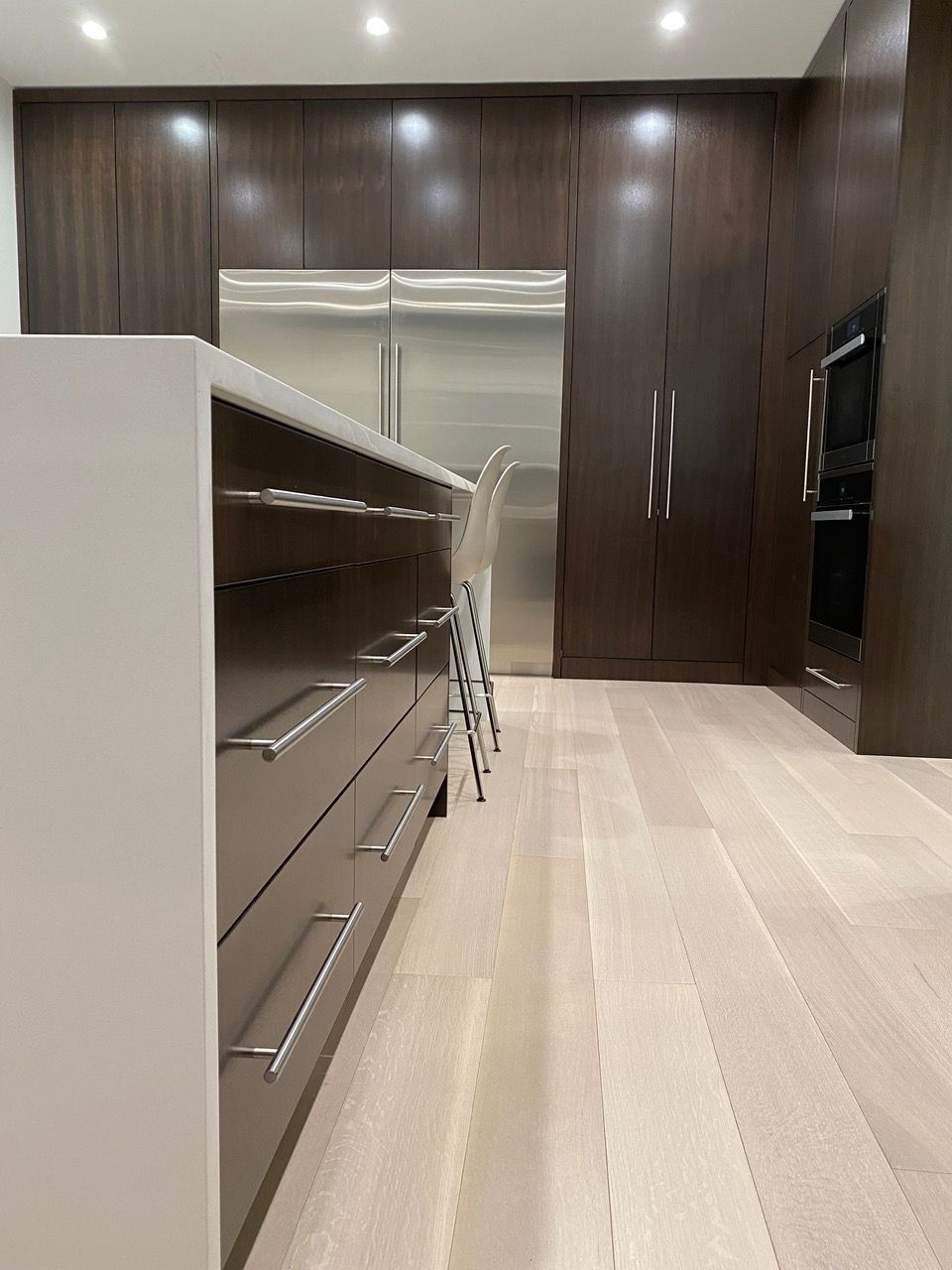 Modern kitchen with dark wood cabinets, stainless steel appliances, and a white island with stools.