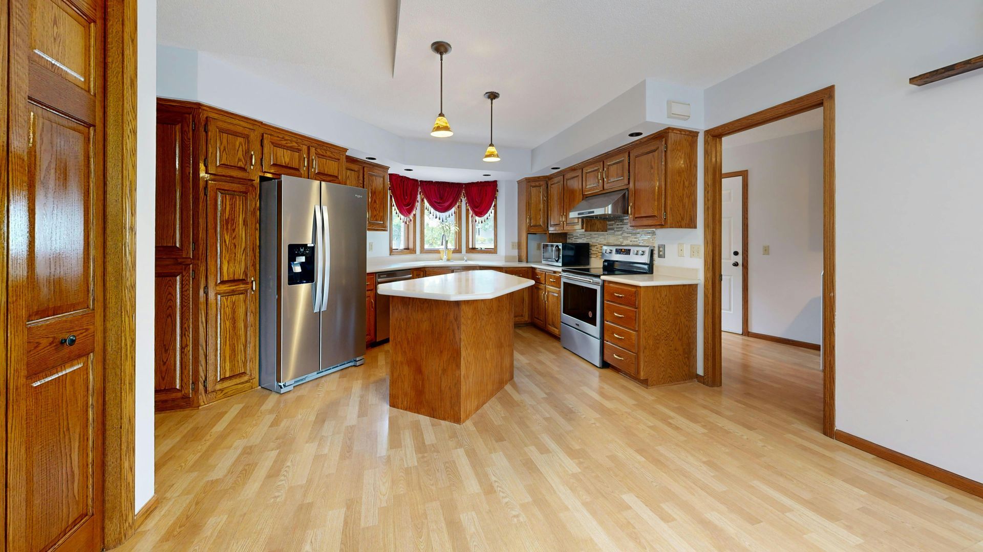 Kitchen with wooden cabinets, stainless steel appliances, and island with pendant lights.