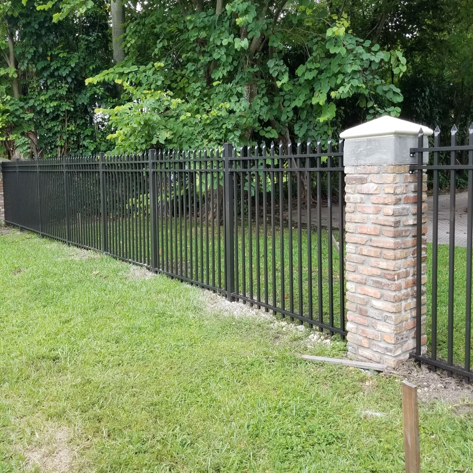 A black metal fence with a brick post in the middle of a lush green field.